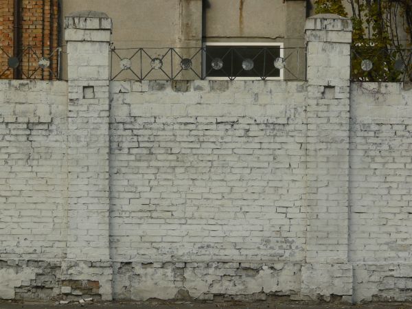 Brick fence texture made up of bricks painted white, with two tall columns made up of similar bricks. Bricks are in various degrees of relief and states of erosion.